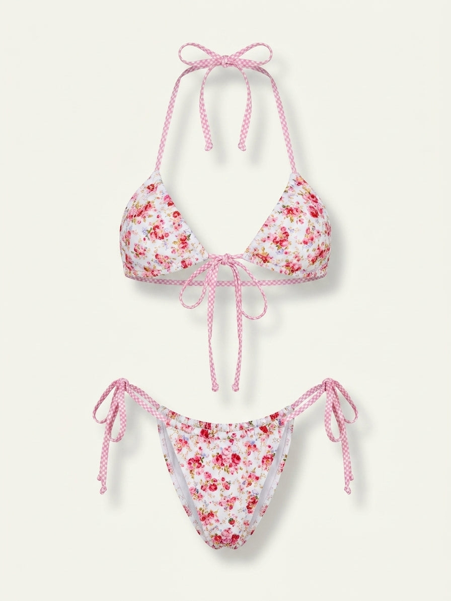 A two-piece bikini set featuring a white base with a red and pink floral print, accented with pink-and-white gingham trim and tie straps, shown against a light cream background.